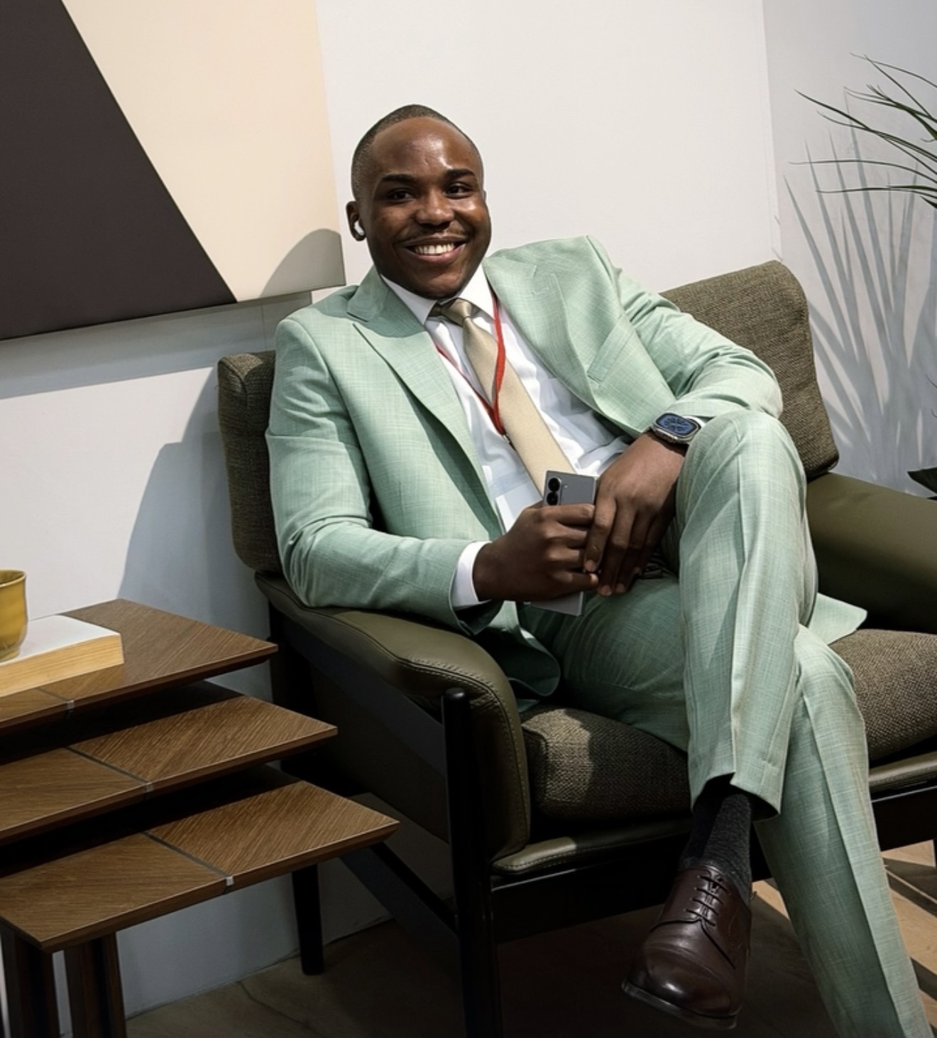 Ekulide Miracle smiling, seated in a mint-green suit